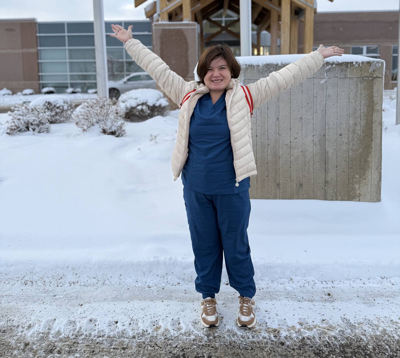 Alyssa in scrubs outside the hospital on a snowy day, arms thrown wide